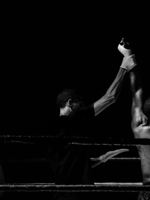 A referee raises the winner's hand in a dark boxing ring
